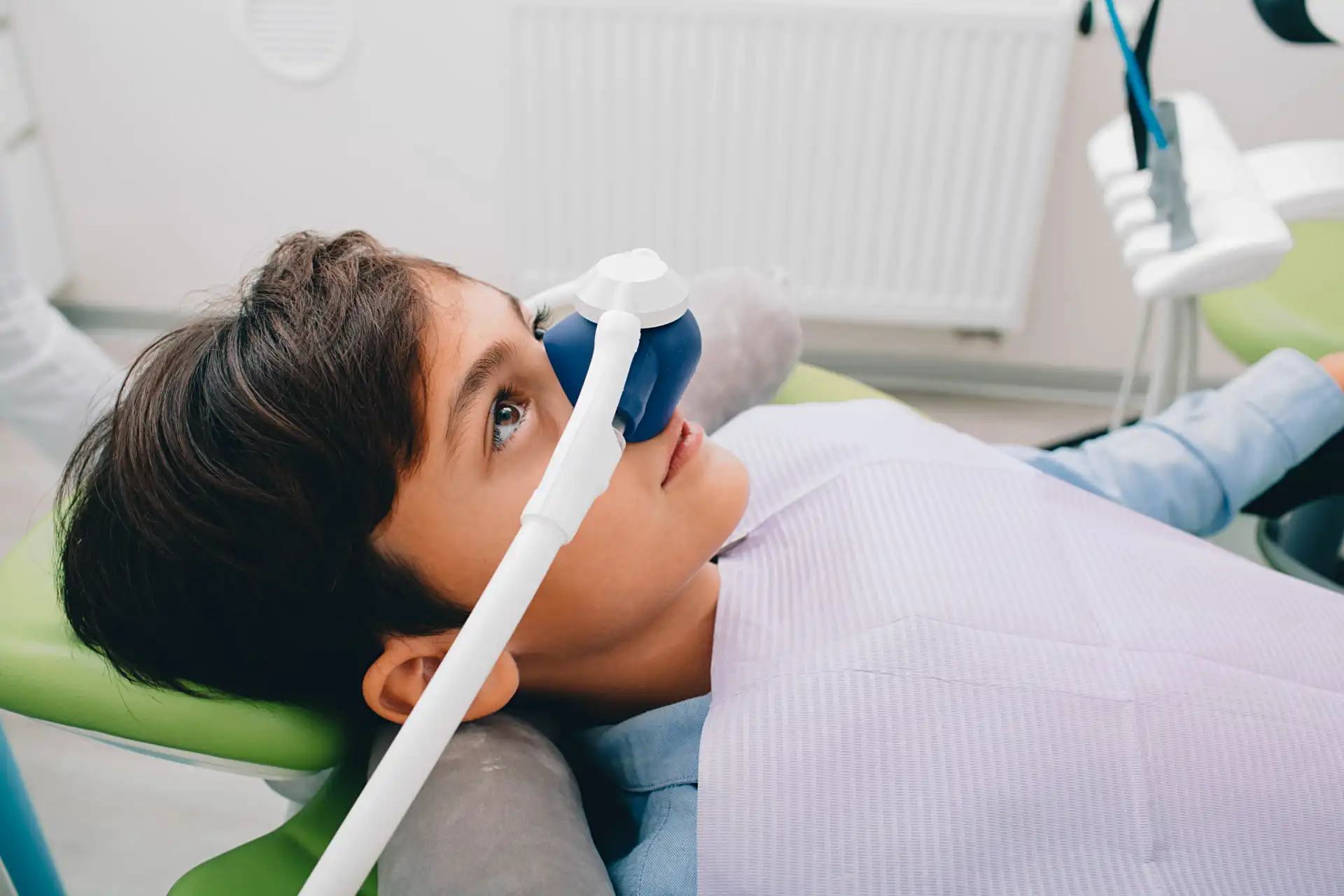 Criança em consulta odontológica, utilizando máscara de sedação com aparelho, em ambiente de clínica dentária